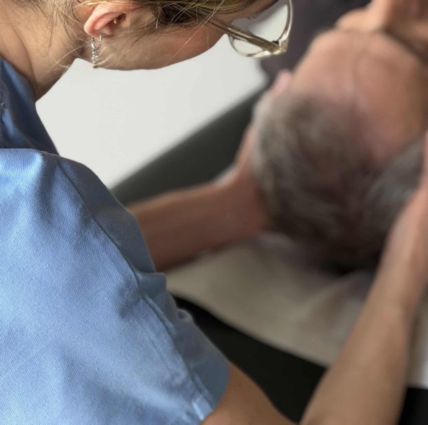 Plan rapproché sur Anna Monlezun, ostéopathe à Montgiscard, effectuant une séance d'ostéopathie crânienne douce sur un patient âgé.